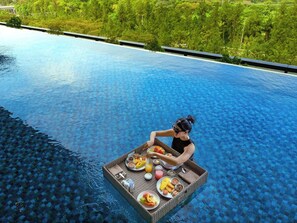 A person sitting on a floating platform in a clear blue pool with a tray of food.