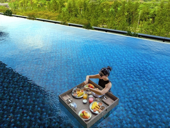 Una persona sentada en una plataforma flotante en una piscina azul cristalina con una bandeja de comida.