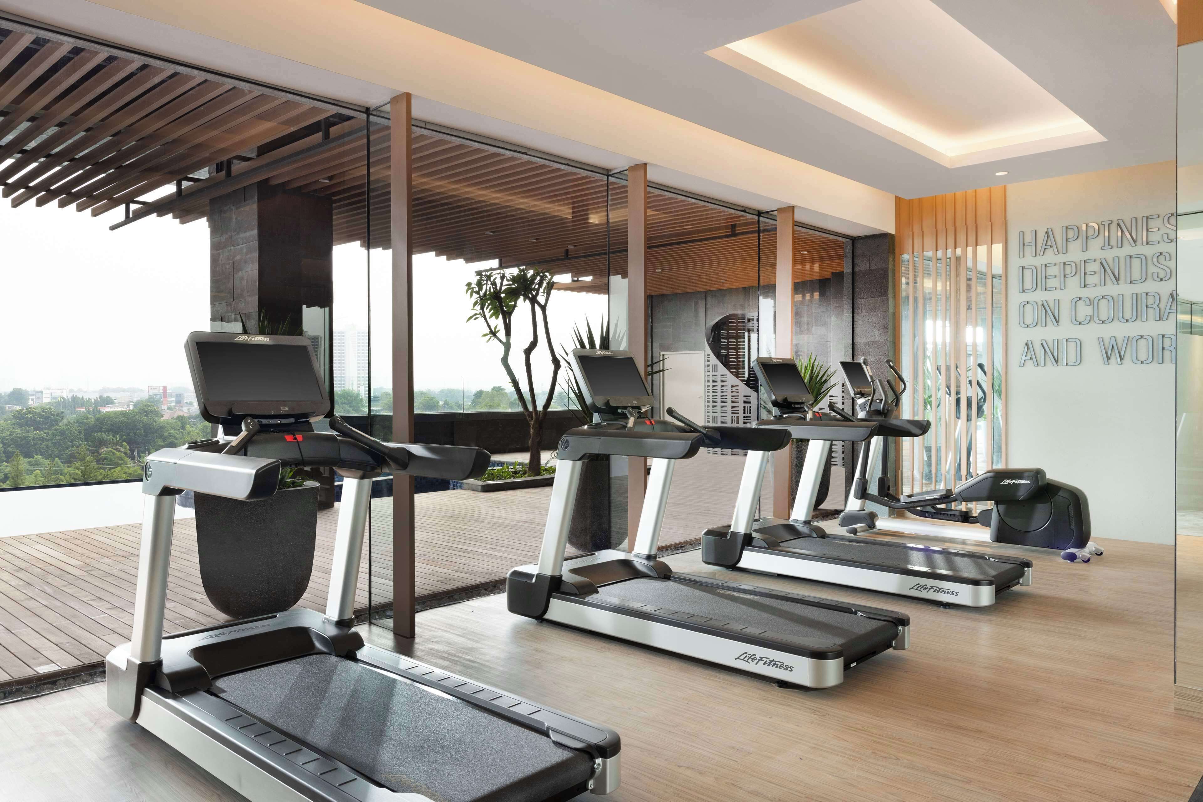 A modern gym with treadmills, exercise bikes, and a motivational quote on the wall.