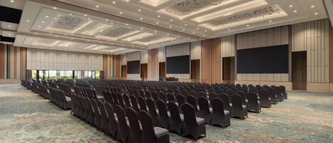 A large conference room with rows of chairs, a podium, and a large screen.
