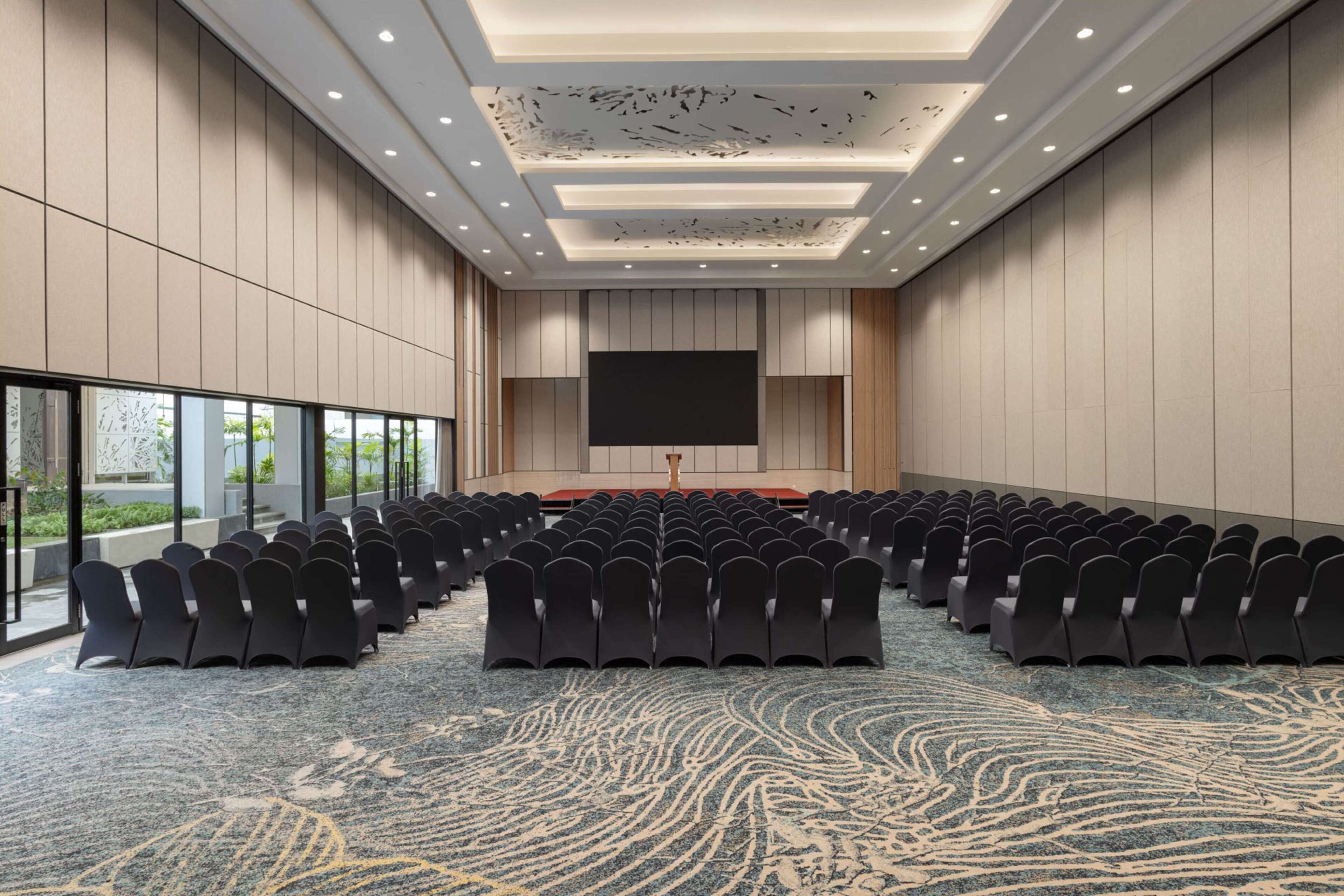 A conference room with rows of chairs, a large screen, and a carpeted floor.