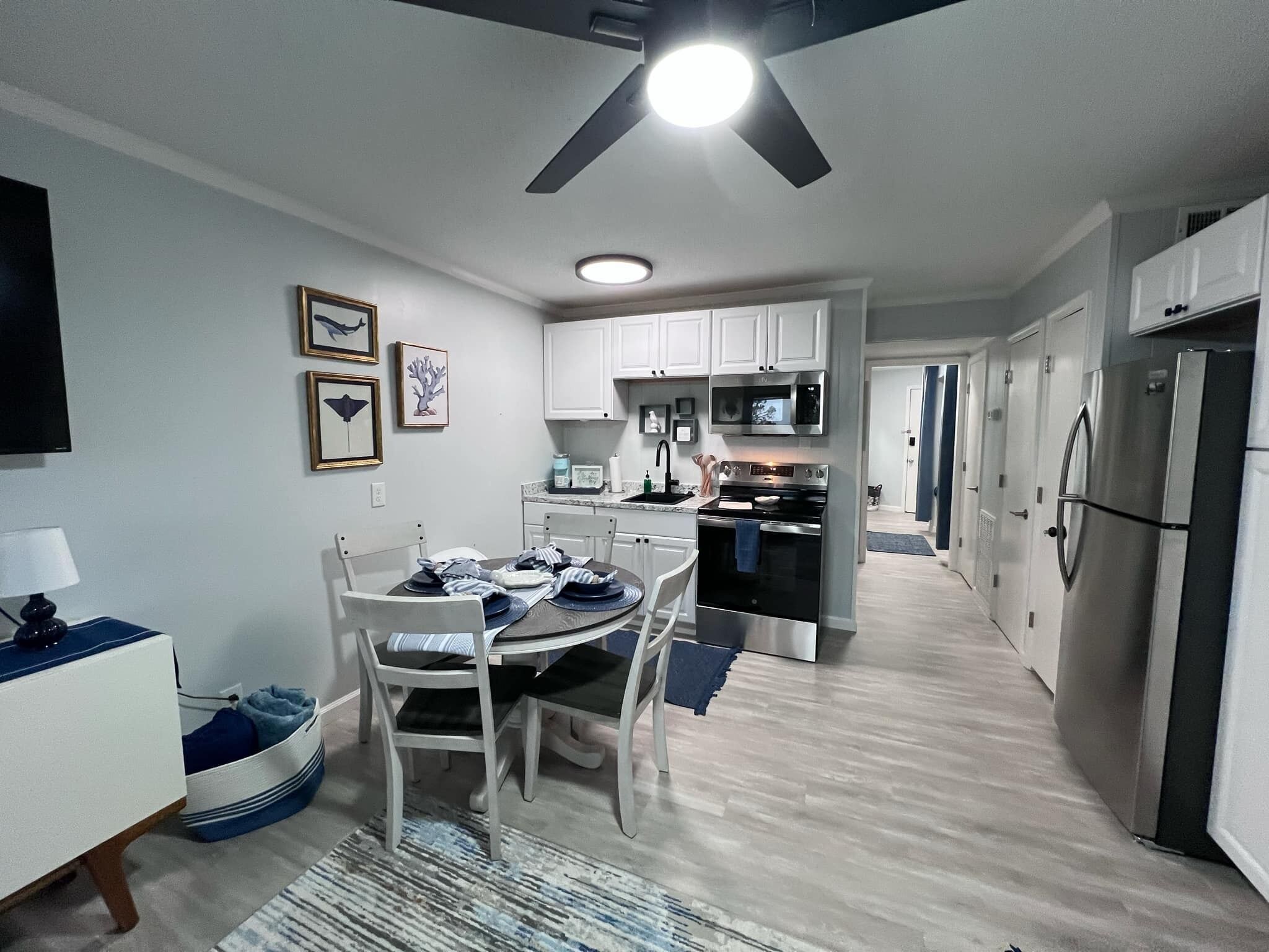 A modern kitchen with white cabinets, a stainless steel refrigerator, and a dining area with a table and chairs.