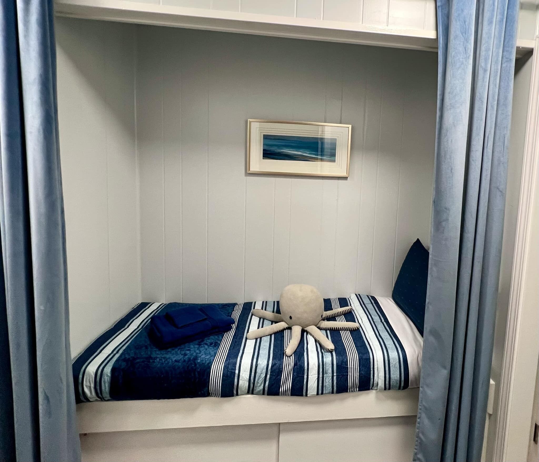 Een stapelbed met een gestreepte dekbedovertrek, een ingelijst beeld aan de muur en een zacht octopusknuffel op het bed.