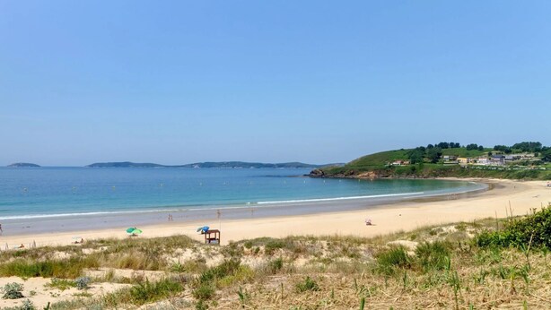 Una playa con arena, algunas sombrillas y una silla.