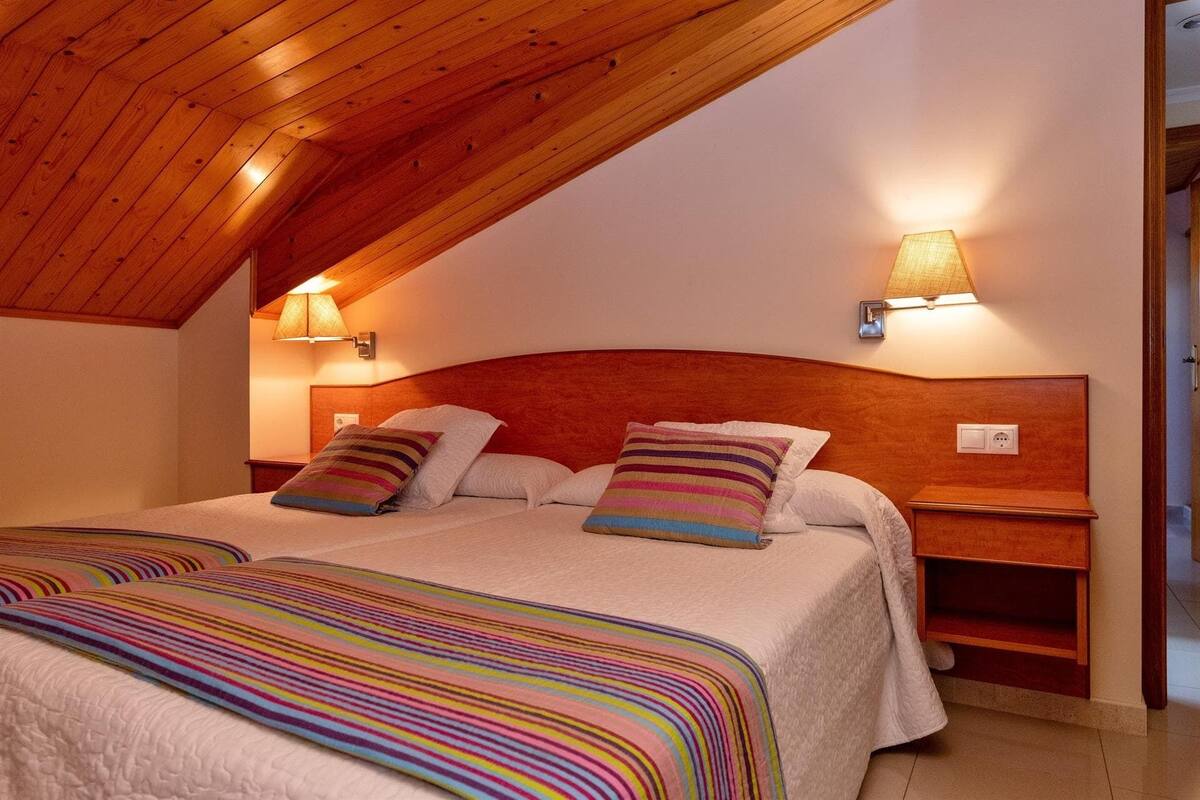Un dormitorio con techo inclinado, cabecera de madera, dos lámparas de noche, cama con ropa de cama a rayas y una mesita de noche.