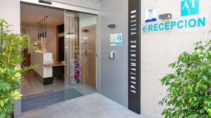 Entrada moderna de un edificio con área de recepción, puertas de vidrio y un cartel que indica 'APARTMENTS VELERO'.