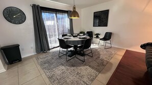 Un comedor con una mesa redonda, sillas, un reloj y un ventanal con cortinas.