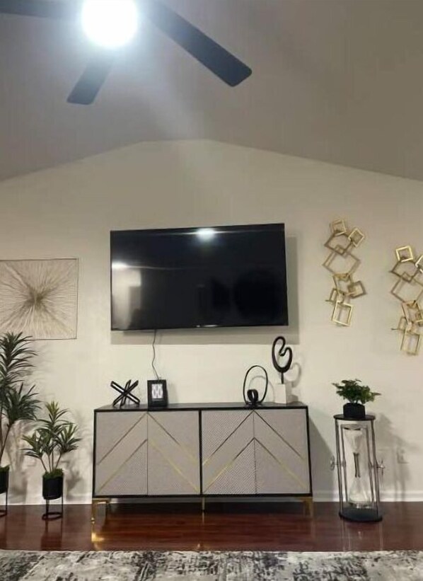 A living room with a flat-screen TV mounted on the wall, a modern cabinet below, and decorative items on the walls.