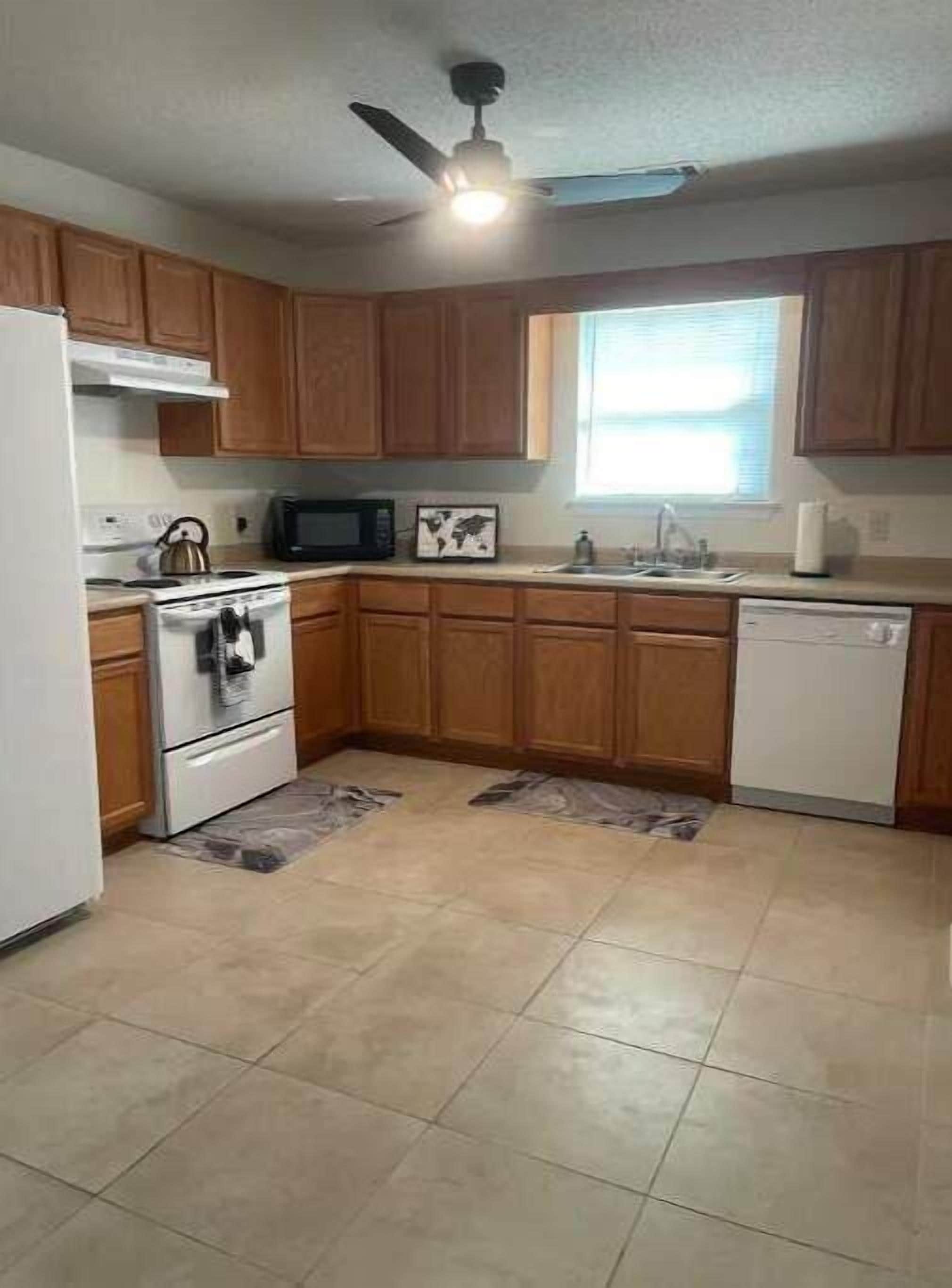 A kitchen with wooden cabinets, a microwave, a stove, a sink, and a ceiling fan.