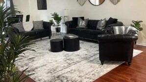 Una sala de estar con ventilador de techo, un sofá negro, una mesa de centro y un espejo grande en la pared.