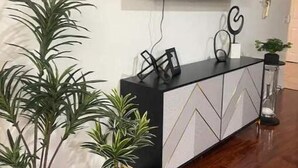 Una sala de estar moderna con un televisor de pantalla plana montado en la pared, un mueble blanco y negro con objetos decorativos, y varias plantas en macetas.