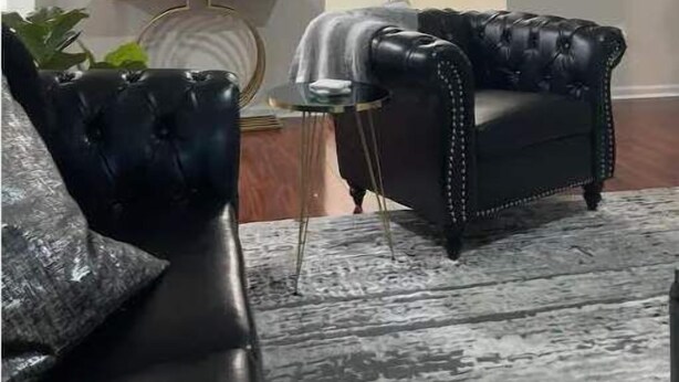 Una sala de estar con un sofá de cuero negro, un espejo redondo y una mesita auxiliar.