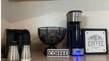 A kitchen counter with a coffee maker, two thermos flasks, a coffee grinder, and a sign that reads "Wake Up The Coffee".