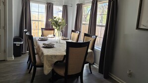 Un comedor con una mesa dispuesta para cuatro personas, un jarrón con flores y cortinas en las ventanas.