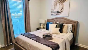 Una cama bien hecha con cabecera, lámpara de noche y ventana con cortinas.
