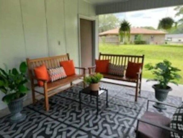 A porch with two wooden benches, a patterned floor, and potted plants.