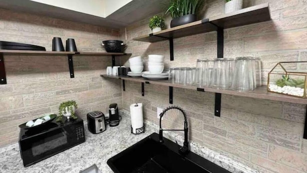 Una cucina moderna con ripiani in granito, elettrodomestici neri e mensole in legno piene di stoviglie e piante.