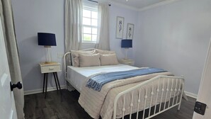 Une chambre à coucher comprenant un lit, deux tables de chevet, une fenêtre avec des rideaux et deux lampes fixées au mur.