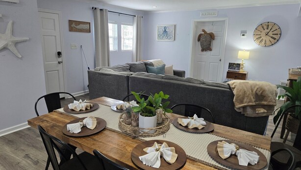 Un coin repas avec une table en bois dressée pour quatre personnes, un canapé gris et une horloge au mur.