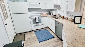 Une cuisine avec des meubles blancs, une cuisinière, un lave-vaisselle et un tapis bleu.