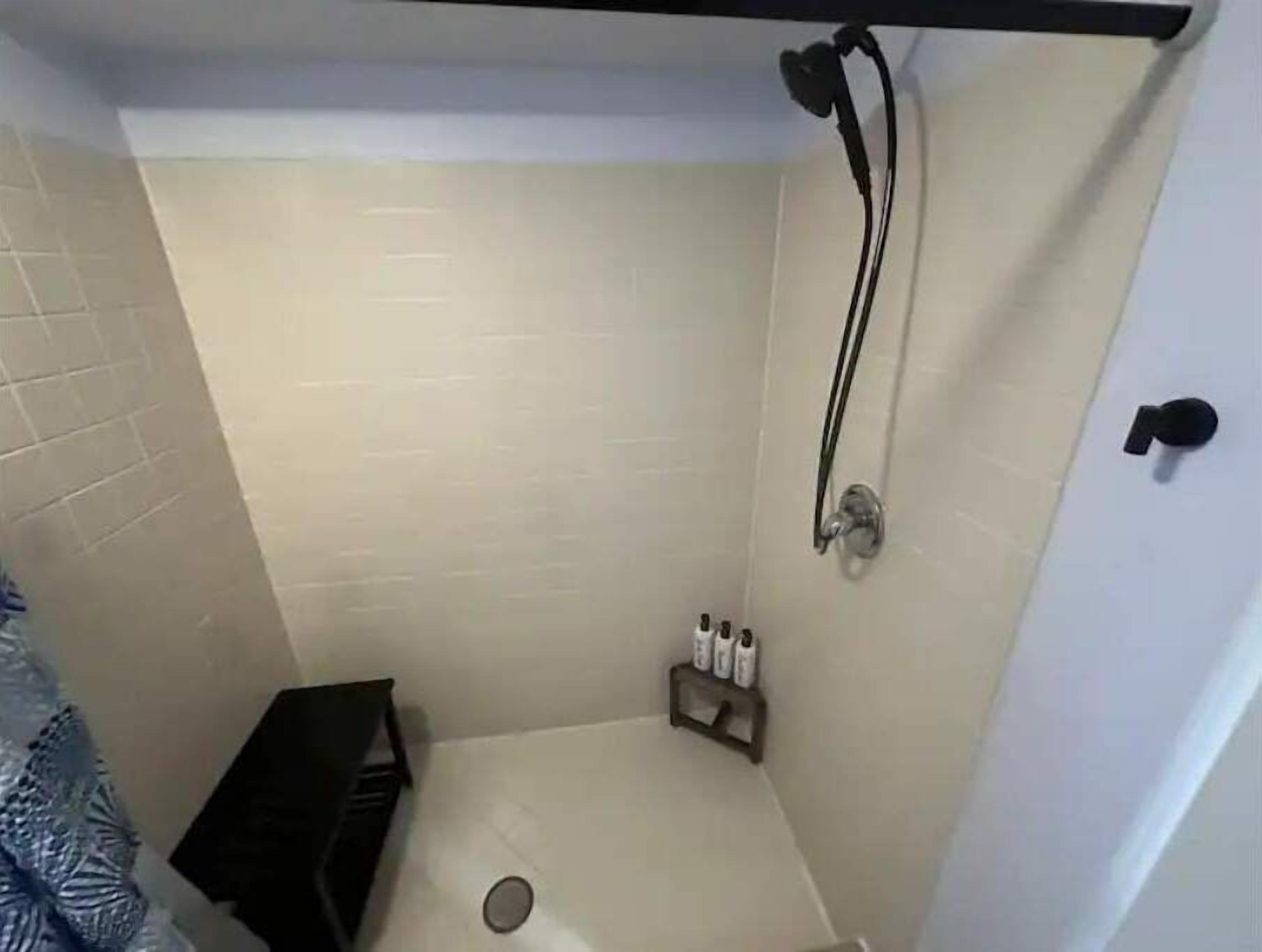 A small, tiled shower room with a showerhead, a towel rack, and a soap dispenser.