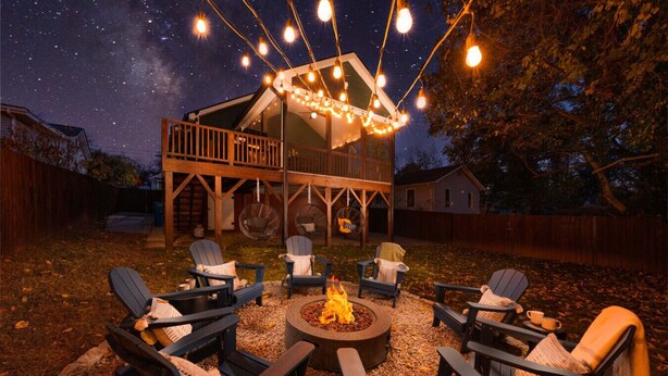 Een terras met Adirondack-stoelen, een vuurkorf en sfeerverlichting.