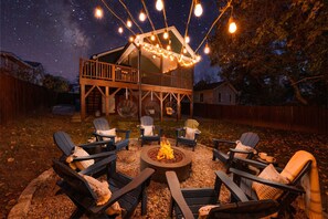 An outdoor seating area with Adirondack chairs, a fire pit, and string lights.
