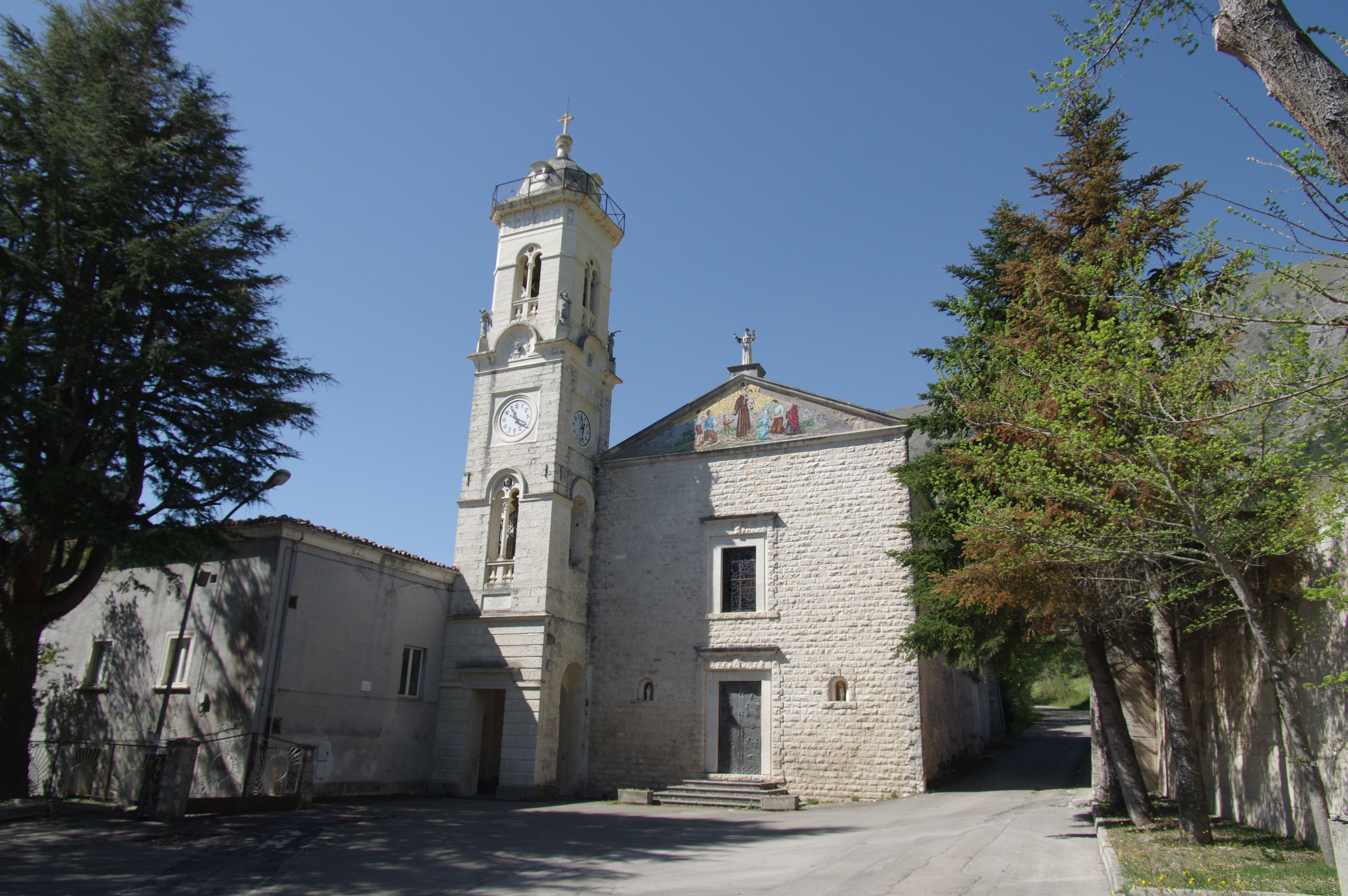 A church with a bell tower and a clock, surrounded by trees and a paved path.