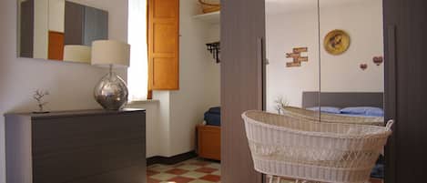 A room with a checkered floor, a dresser, a lamp, a crib, and a mirror on the wall.