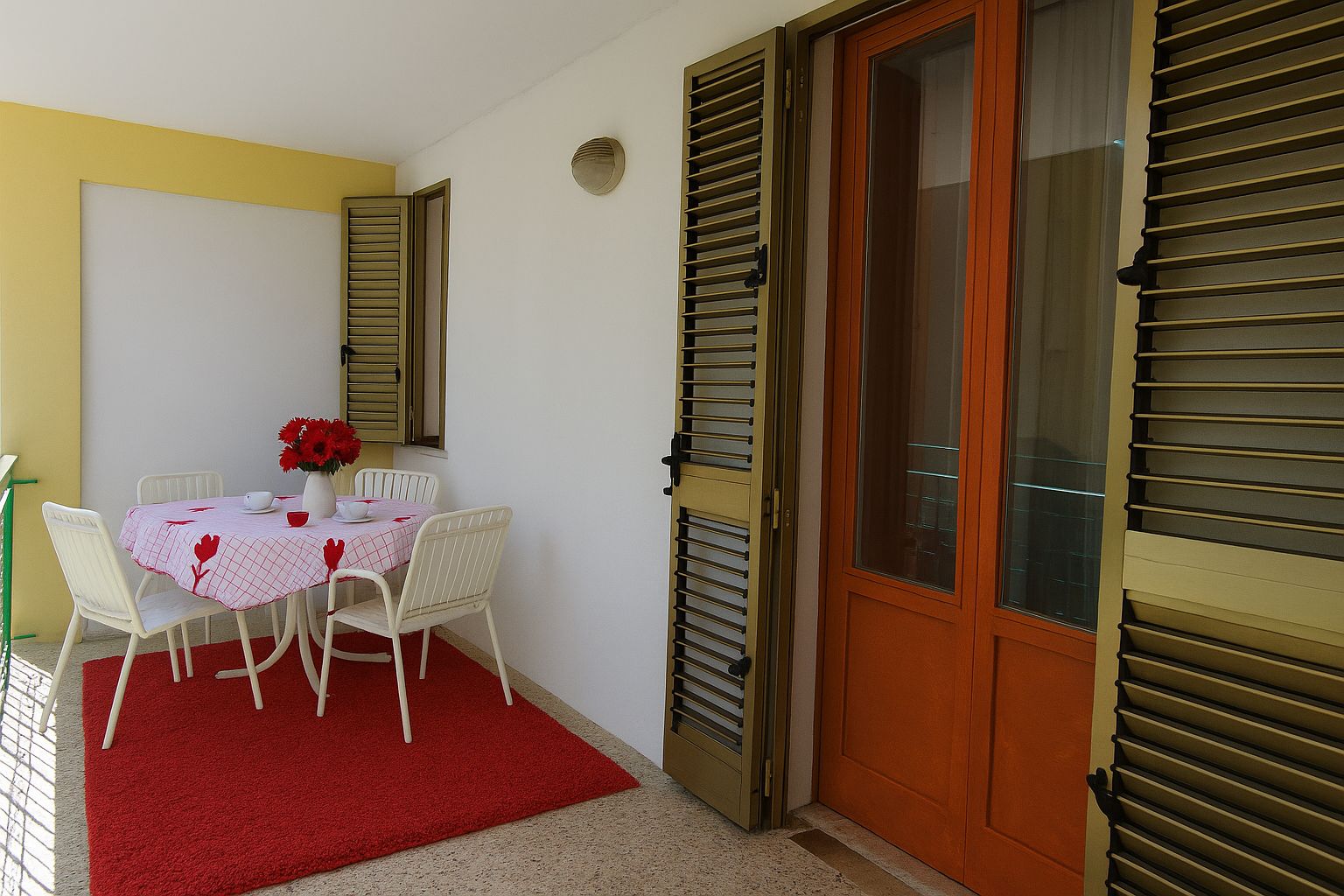 Une pièce avec une table à manger dressée pour deux personnes, une moquette rouge et une porte à volets.