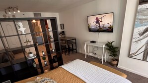 Ein Hotelzimmer mit einem großen Bett, einem an der Wand montierten Fernseher, einem Schreibtisch und einer Sitzecke mit Sofa und Sesseln.