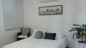 Une chambre bien rangée, avec un lit, une chaise, une plante en pot et un tableau encadré au mur.