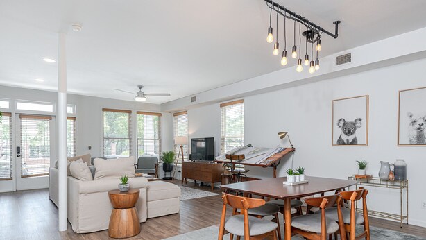 A spacious living room with a sofa, coffee table, dining table with chairs, a TV, and artwork on the walls.