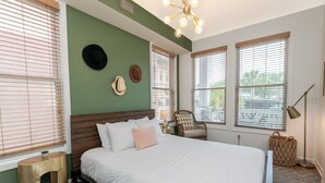 A bedroom with a bed, a chair, a lamp, and a window with blinds.