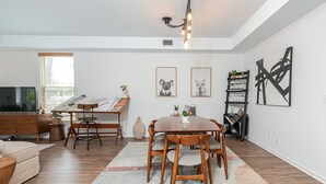 A modern living room with a dining area, wooden furniture, a television, and artwork on the walls.