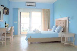 Un dormitorio con cama, escritorio y silla. Hay un televisor en la pared y una ventana con cortinas.