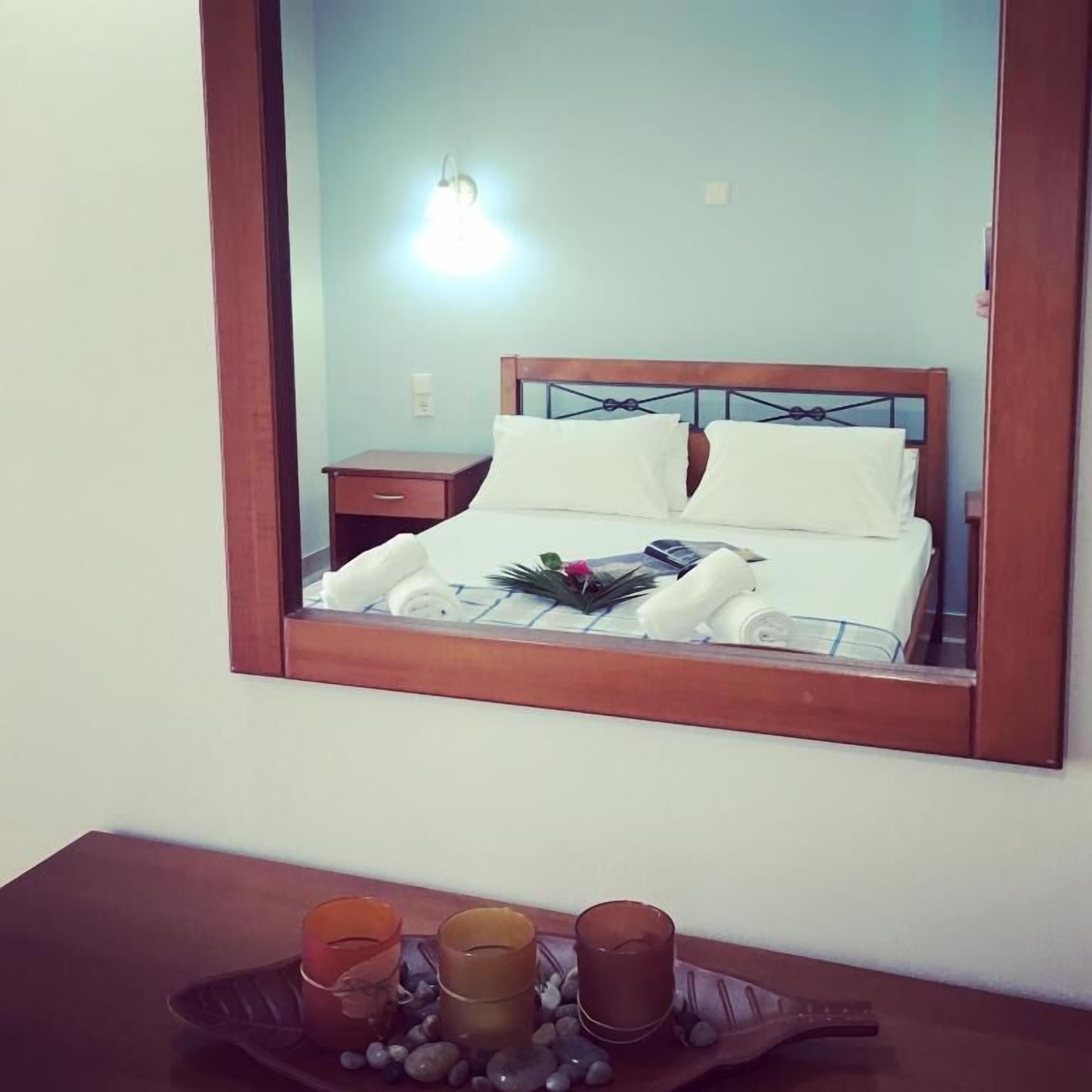Un lit bien fait, avec du linge de lit blanc et des oreillers, une table de chevet avec une lampe, et un plateau avec des bougies et des pierres.