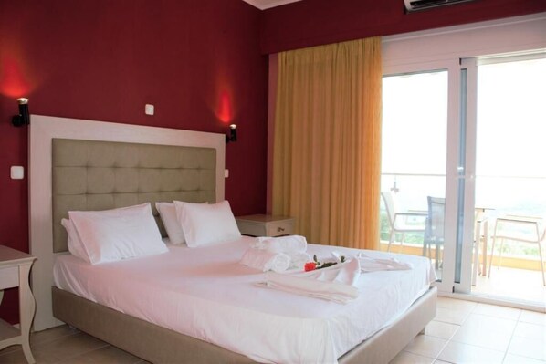 A hotel room with a large bed, a nightstand, a desk, and a balcony with chairs.