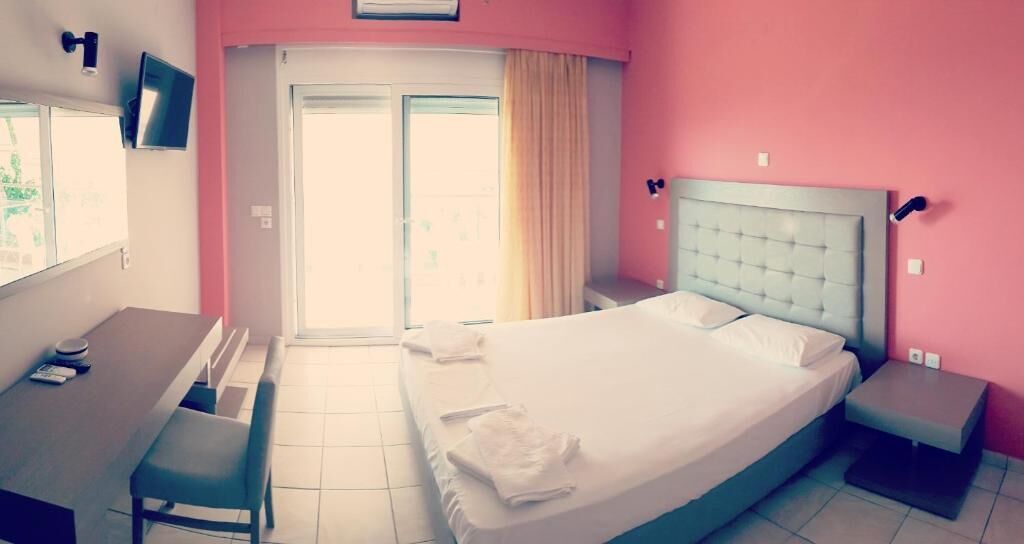 A hotel room with a bed, a desk, a chair, a small table, and a window with curtains.