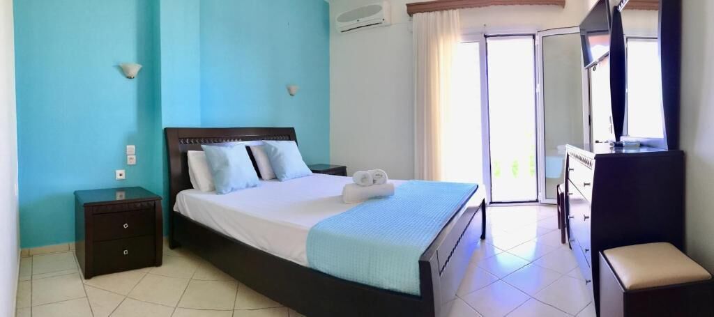 Une chambre d’hôtel avec un lit, une table de chevet, une commode et une fenêtre avec des rideaux.