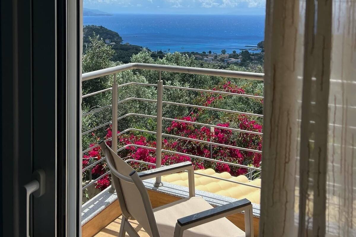 A balcony with a metal railing, a beige chair, and vibrant pink flowers.