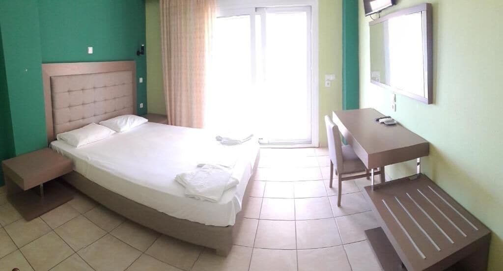 A hotel room with a bed, a desk, a chair, a mirror, and a window with curtains.
