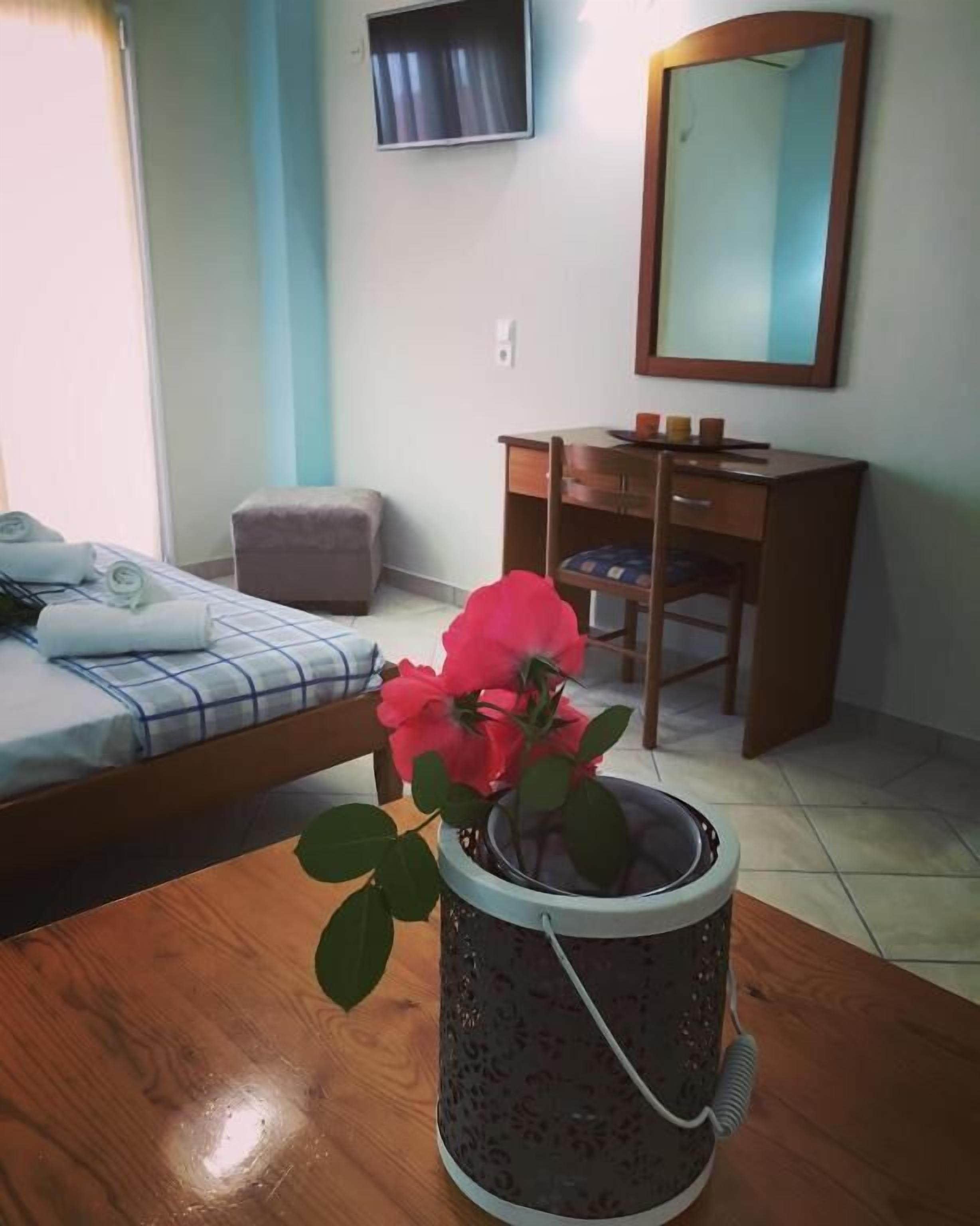 Una habitación con una cama, un escritorio, una silla, una mesita con una planta en maceta y un espejo en la pared.