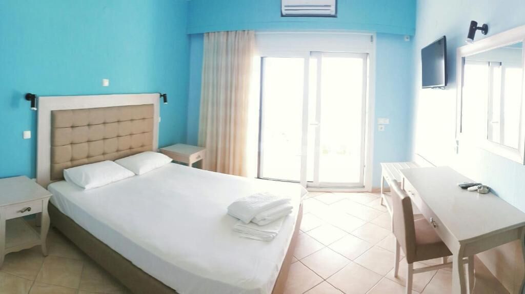 A hotel room with a bed, bedside tables, a desk, a chair, a television, and a sliding glass door to the outside.
