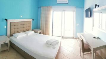 A hotel room with a bed, bedside tables, a desk, a chair, a television, and a sliding glass door to the outside.