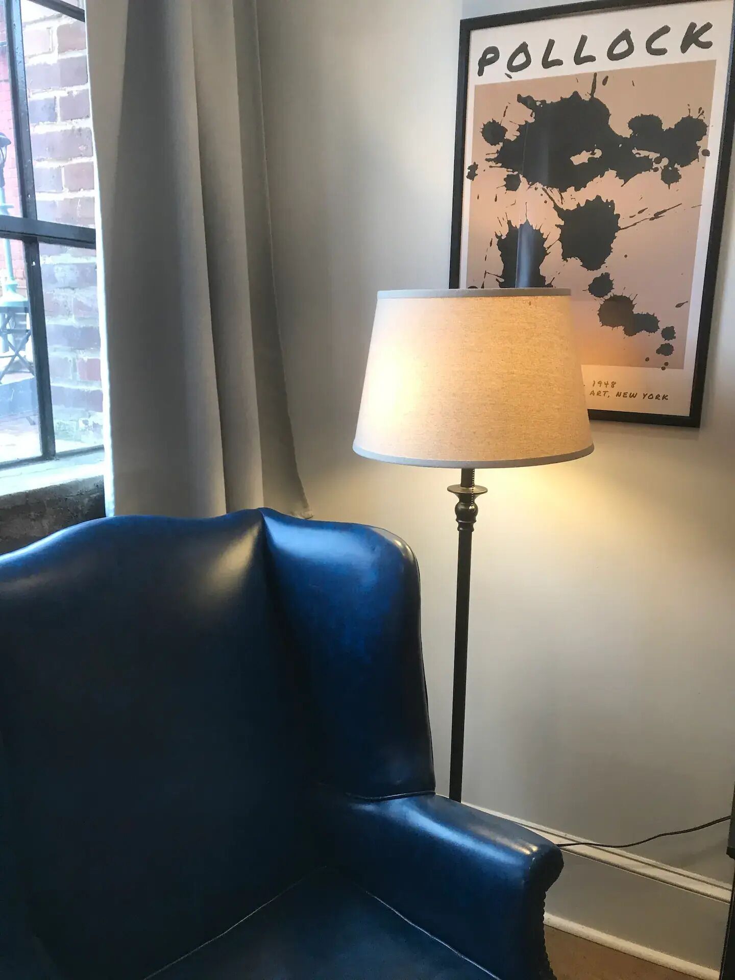 Um quarto com uma poltrona de couro azul, um abajur e uma obra de arte emoldurada na parede.