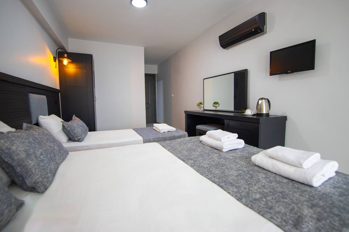 A modern hotel room with two beds, a flat-screen TV, a mirror, and a small table with a kettle.