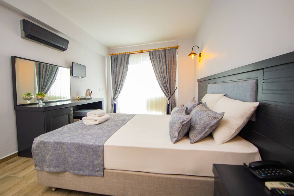 A neatly made bed with a grey and white color scheme, a bedside table with a phone, and a wall-mounted TV.