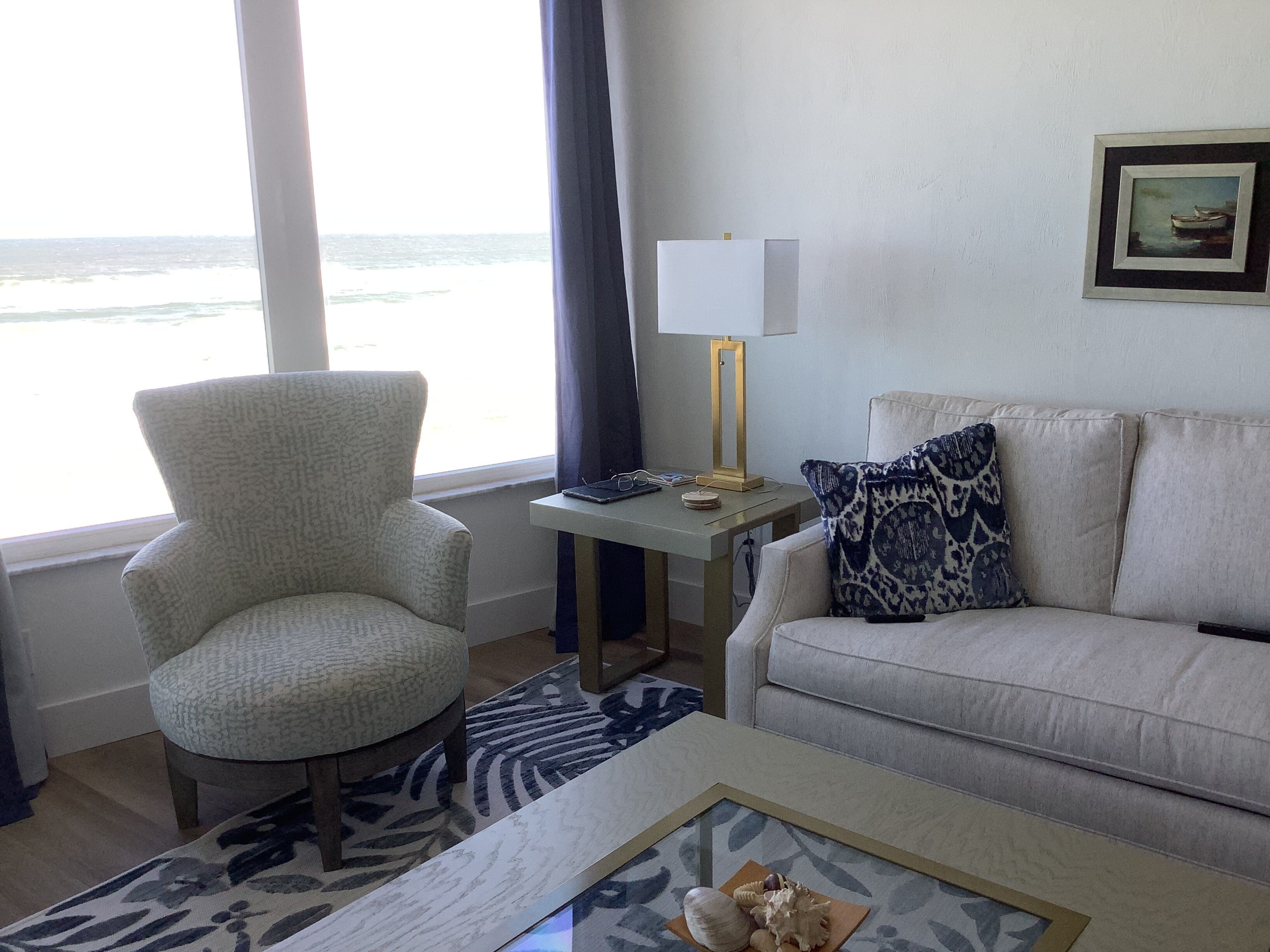 Una sala de estar con vista al océano, un sillón, un sofá, una mesa de centro y una lámpara.
