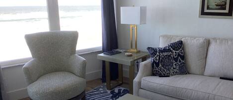 Una sala de estar con vista al océano, un sillón, un sofá, una mesa de centro y una lámpara.